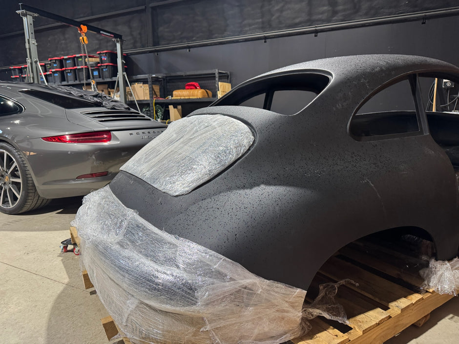 Car body on a wooden pallet with protective covering, surrounded by other cars and equipment.