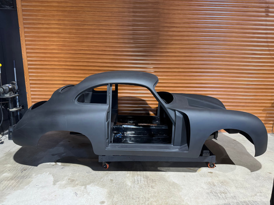 Black car chassis on a concrete floor with a wooden wall in the background