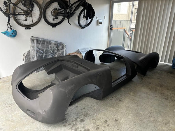 Car body shell on a concrete floor in a garage with bicycles on the wall.