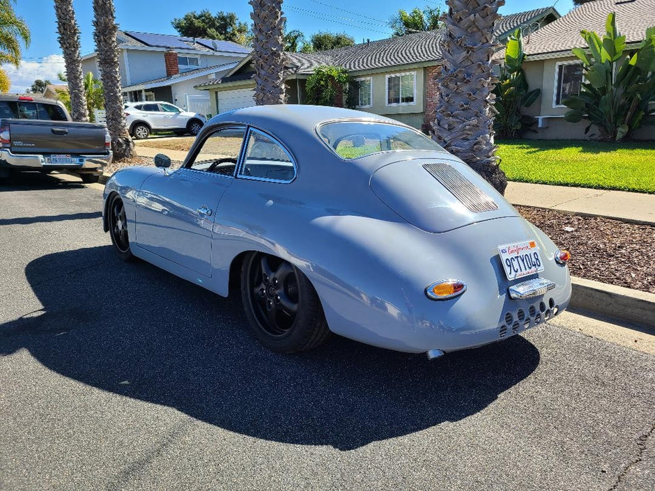 Vintage car parked on a residential street with palm trees and houses in the background.